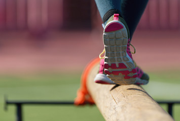 The feet of a athlete as she's walking on a wooden beam outside in the park