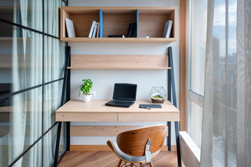 Workplace with laptop on the table. Comfortable work table in office near the window. Design of workplace in home office with modern equipment and objects