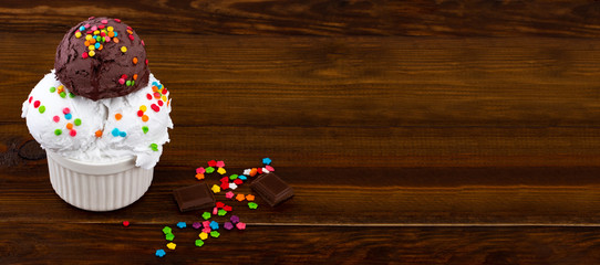 plate of vanilla and and chocolate ice cream scoop swith sprinkles and waffle cones on wooden background with copy space