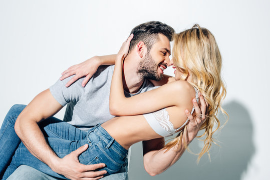 cheerful man looking at happy blonde woman while hugging on white