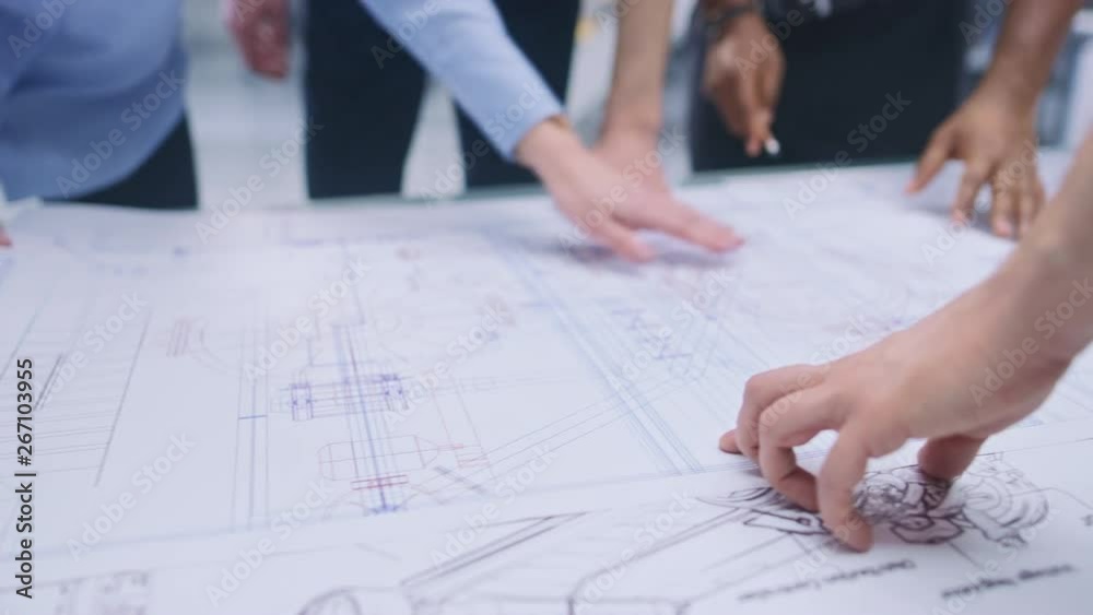 Poster In the Industrial Engineering Facility: Diverse Group of Engineers and Technicians on a Meeting Gather Around Table Unravel Sheets of Engine Design Technical Drafts, Analyse Drawings. Focus on Hands