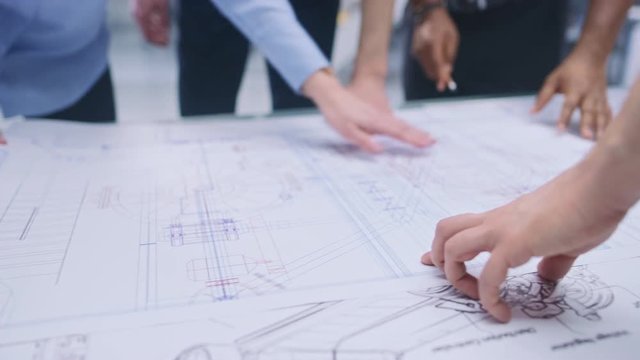In the Industrial Engineering Facility: Diverse Group of Engineers and Technicians on a Meeting Gather Around Table Unravel Sheets of Engine Design Technical Drafts, Analyse Drawings. Focus on Hands