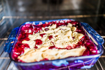 Closeup of hot red cherry cobbler in glass baking pan dish inside on oven rack with bubbles and golden pie crust