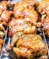 Many roasted whole chicken closeup on tray in deli store shop grocery display brown with herbs, spices on crispy skin