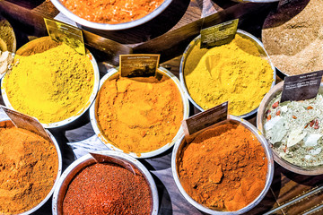 Many spices flat lay top view down on display in bowls trays filled with herbs, signs, curry, turmeric, mixes in store market bazaar