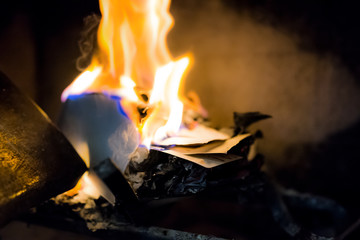 Burning paper, letters in indoor home interior fireplace with closeup of orange and blue fire flame