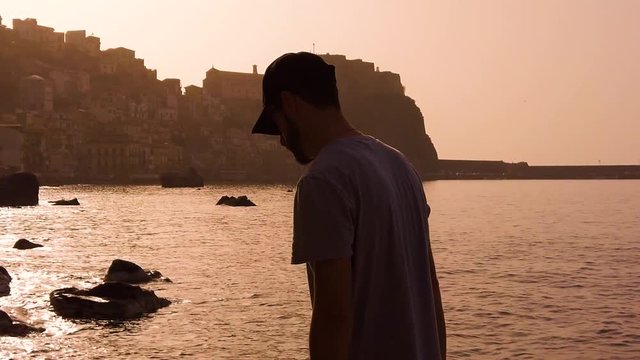 Silhouette di un ragazzo che cammina tra gli scogli vicino a un borgo sul mare. Scilla. Video al rallentatore.