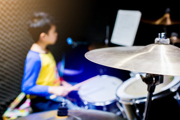 wooden drumsticks in hands of Asian kid wearing blue and yellow t-shirts to learning and play drum set in music room