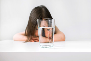 Little girl does not want to drink water. The girl sits at the table upset. The girl is sad because...