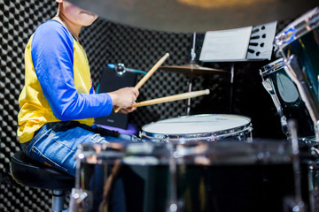 selective focus of wooden drumsticks in hands of Asian kid wearing blue and yellow t-shirts to learning and play drum set in music room