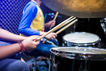 Fototapeta na wymiar hands of teacher with wooden drumsticks guiding boy in drum learning tutorial in recording studio at music academy