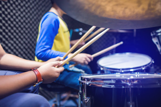hands of teacher with wooden drumsticks guiding boy in drum learning tutorial in recording studio at music academy