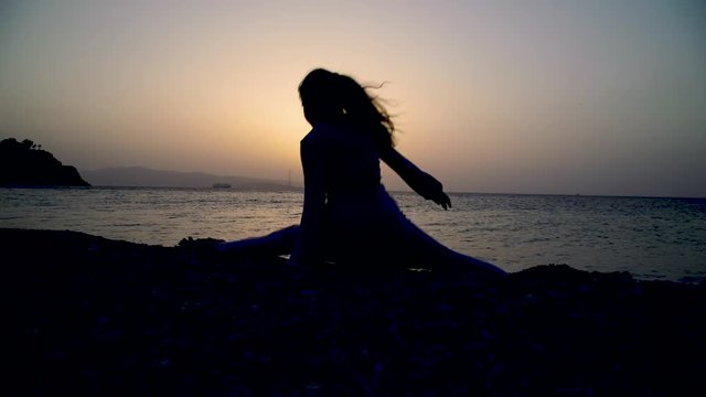 Silhouette di una bambina che fa passi di danza al tramonto sulla spiaggia di fronte al mare.
