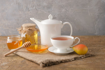 A cup of tea, a white kettle, pears, jars and a saucer with honey on the table. Morning breakfast.