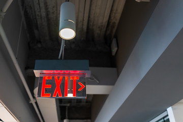 Red exit sign hanging from ceiling looking up view with arrow direction and color illuminated...