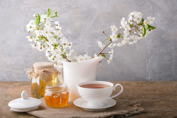 A cup of tea, a white kettle with cherry blossoms, jars of honey on the table. Morning breakfast.