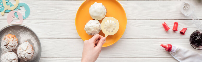 panoramic shot of woman decorating cupcakes on plate with baking stencil