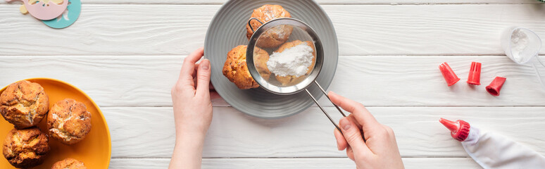 panoramic shot of woman decorating cupcakes with powdered sugar and sieve on white table