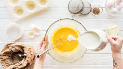 Cropped view of woman pouring milk in liquid dough on table with ingredients