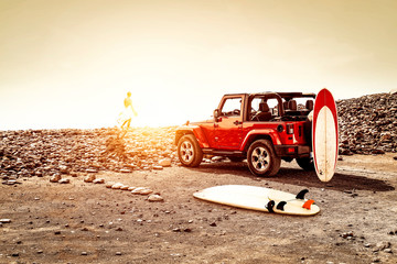 Fototapeta na wymiar Red summer car on beach and free space for your decoration. Sunset time and surfer. 