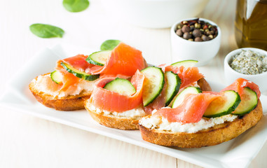 Salmon, cucumber and cream cheese bruschetta. Italian tapas, antipasti with vegetables, herbs and oil on grilled ciabatta and baguette bread. Sandwich.
