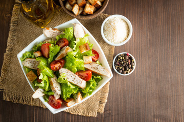 Fresh salad made of tomato, ruccola, chicken breast, eggs, arugula, crackers and spices. Caesar salad in a white, transparent bowl on wooden background