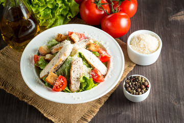Fresh salad made of tomato, ruccola, chicken breast, eggs, arugula, crackers and spices. Caesar salad in a white, transparent bowl on wooden background