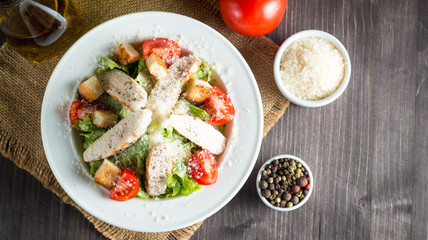 Fresh salad made of tomato, ruccola, chicken breast, eggs, arugula, crackers and spices. Caesar salad in a white, transparent bowl on wooden background