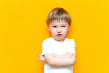 Portrait of angry little boy with arms folded isolated on yellow background. Sad and unhappy child. Upset toddler boy