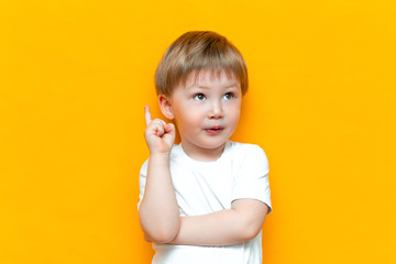 Portrait of cute handsome blonde little boy with finger pointed up. Little child has idea. Kid isolated on yellow blackground. Success, bright idea, creative ideas