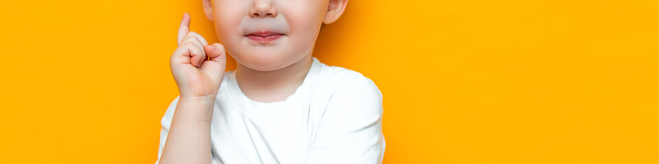 Fototapeta premium Portrait of cute handsome blonde little boy with finger pointed up. Little child has idea. Kid isolated on yellow blackground. Success, bright idea, creative ideas