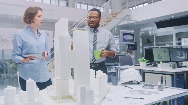 In Architectural Bureau: Architect and Engineer Talking, Working on a Building Complex Prototype Project, Using City Model and Computers Running 3D CAD Software. Residential or Business District