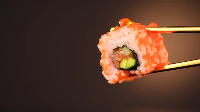 Sushi roll in chopsticks over black background. Seafood. Healthy eating, dieting concept. 4K UHD video footage. 3840X2160