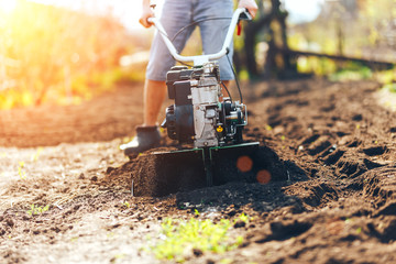 close up photo of young farmer gardener cultivate ground soil rototiller , tiller tractor, cutivator, miiling machine, prepare for planting crop, spring. modern farming, technology agriculture - obrazy, fototapety, plakaty