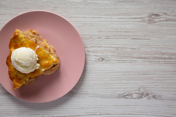 Top view, slice of homemade apple pie with ice cream on a pink plate over white wooden surface, top view. Copy space.