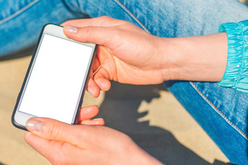 Image Mockup of beautiful hands of a woman holding a white mobile phone with a blank screen on her hip on the beach, on the sand. Close up.