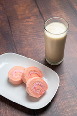 Strawberry cake roll on white dish and milk with wood background.