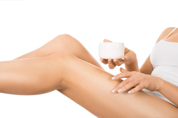 Female legs and hands with a jar of cream. Woman applying moisturizer on her perfect legs, isolated on white background.