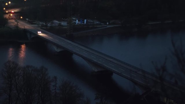 Cars driving over a bridge at night. Street lamps are reflecting in the water.