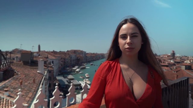 Young beautiful brunette woman in a red dress on a background of blue sky and river, roof Venice, Italy