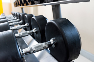 Fototapeta na wymiar Black dumbbell set on rack close up in sport fitness center weight training equipment concept