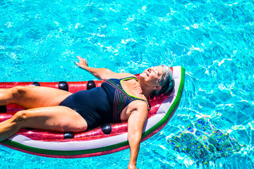 Happy beautiful aged senior lady enjoy the fresh water on a watermelon coloured lilo inflatable...