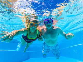 Adult people senior couple have fun swimmin in the pool underwater with coloured funny diving masks - dive concept and active retired man and woman enjoying the lifestyle - blue water and adults