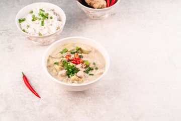 green chicken curry on a bowl, on a light grey marble backdrop, bowl of rice, ginger and chillies on background
