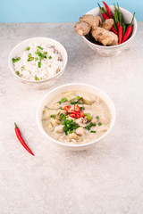 green chicken curry on a bowl, on a light grey marble backdrop, bowl of rice, ginger and chillies on background