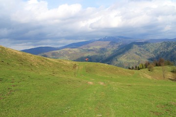 A girl in a bright coat standing on a hill on the background of mountains