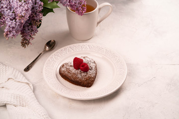 heart shaped cake on a white plate on alight backdrop, cup of tea and lilac on background
