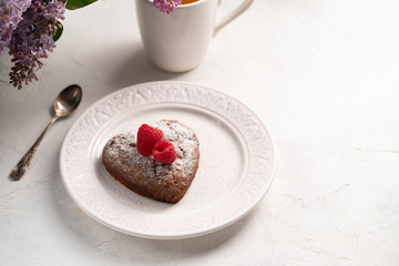 heart shaped cake on a white plate on alight backdrop, cup of tea and lilac on background