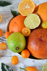 Citrus assortment in a bowl against the white wooden background. Red orange, lime, lemon and kumquats