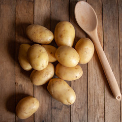 Pile of potatoes and wooden spoon on old wooden table. Top view.
